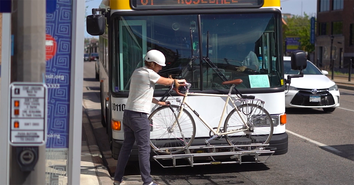 A person puts their bike on a Metro Transit bus, using the rack at the front end of the bus.