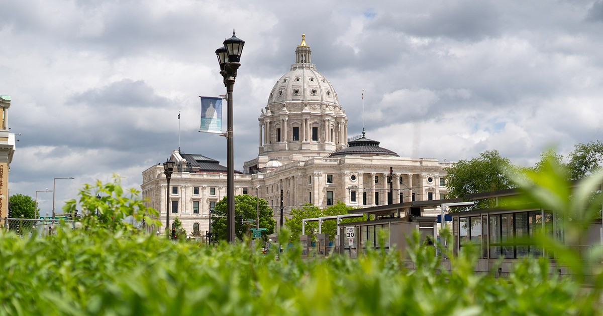 A view of the Minnesota State Capitol building with greenery in the foreground and cloudy skies overhead.