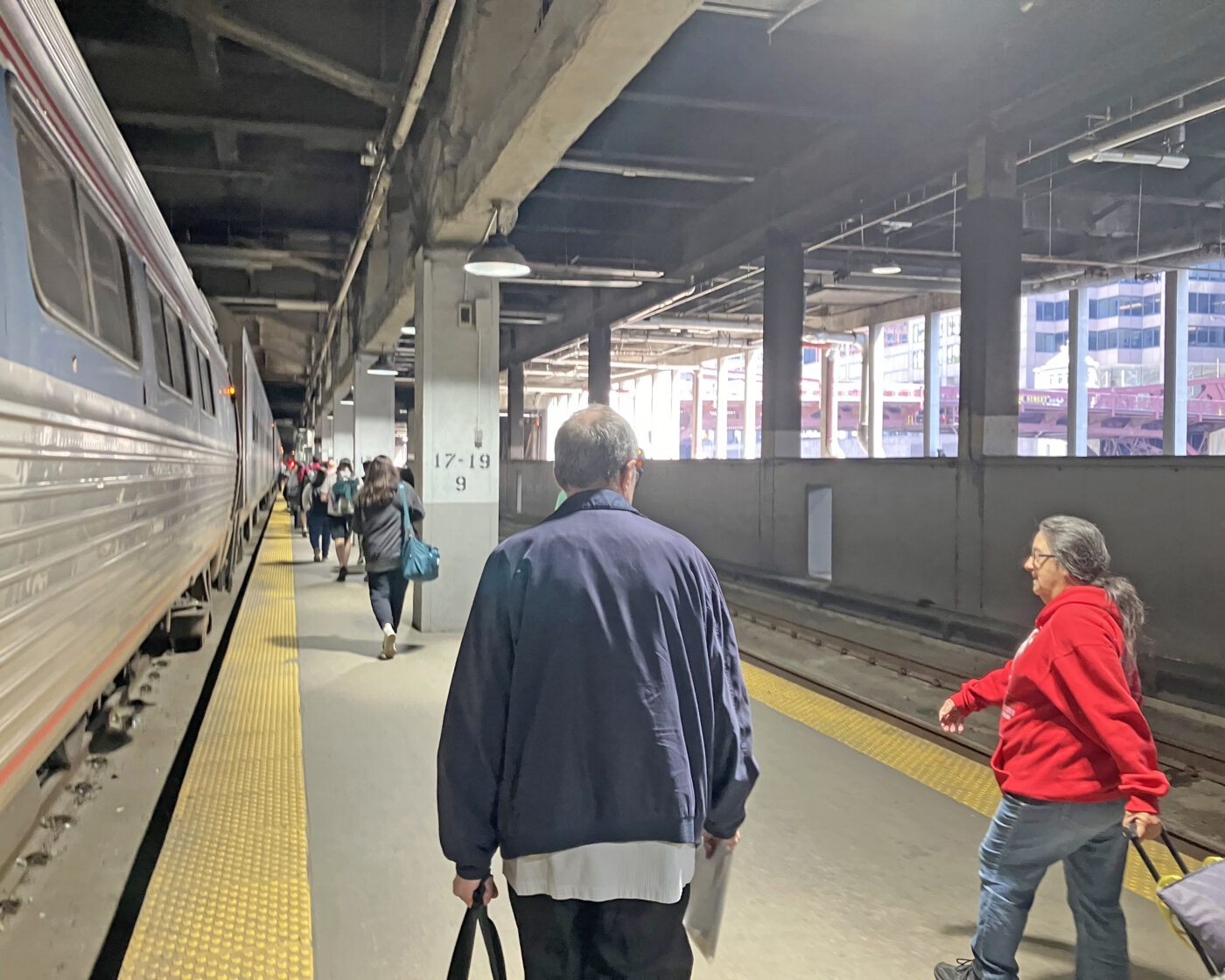 An indoor train platform with several passengers walking alongside the train cars