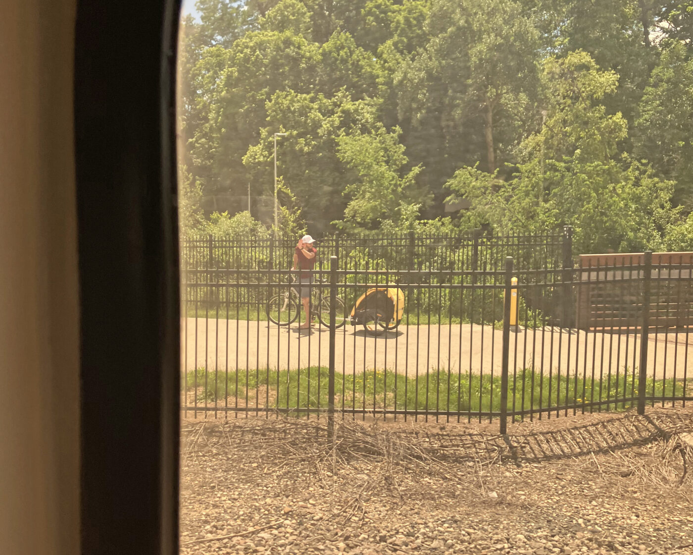 A man on a bicycle with a yellow trailer waving at the train