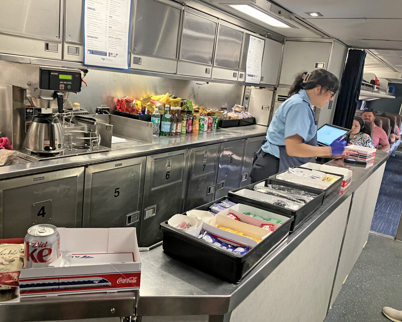 A train cafe car with a woman preparing sandwich boxes for passengers