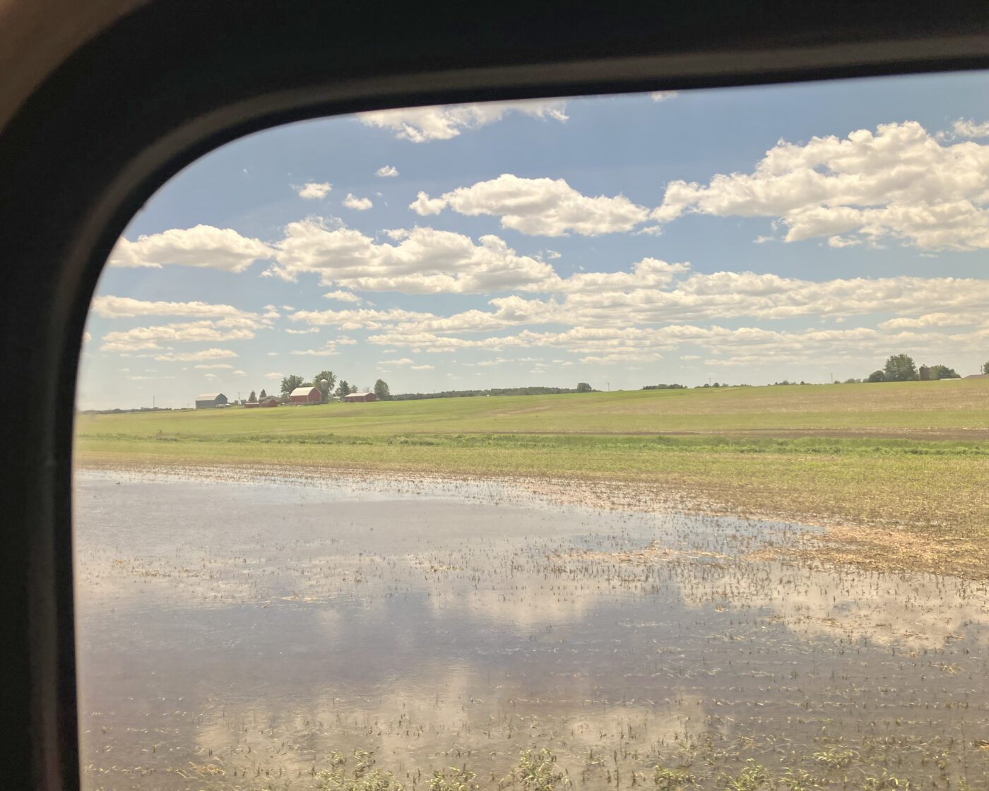 A blue sky with white clouds over farms land and a red farmhouse 