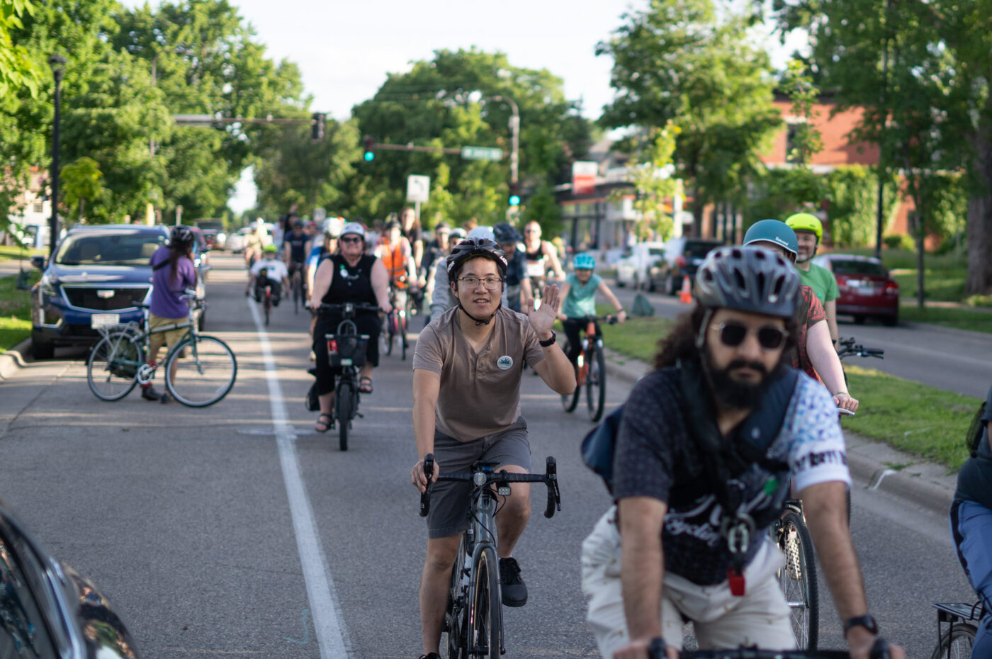 A group of bicyclists on a city street, one raising his arm to the camera