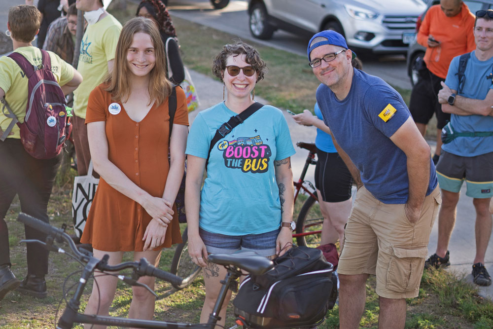 Three advocates, standing behind a bicycle, smile at the camera at the Livable Lyndale rally