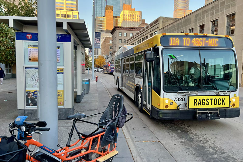 A bus drives down Nicollet Mall at dusk, passing a bicycle with a child seat parked in front of a covered stop