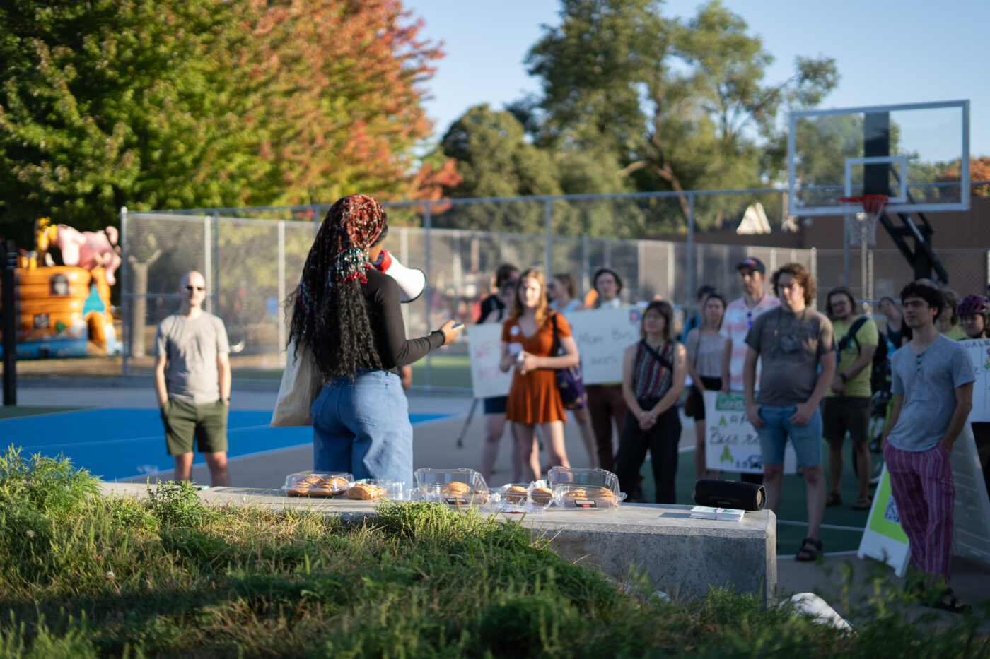 A young Black woman with a colorful headscarf speaks to the crowd through a megaphone 