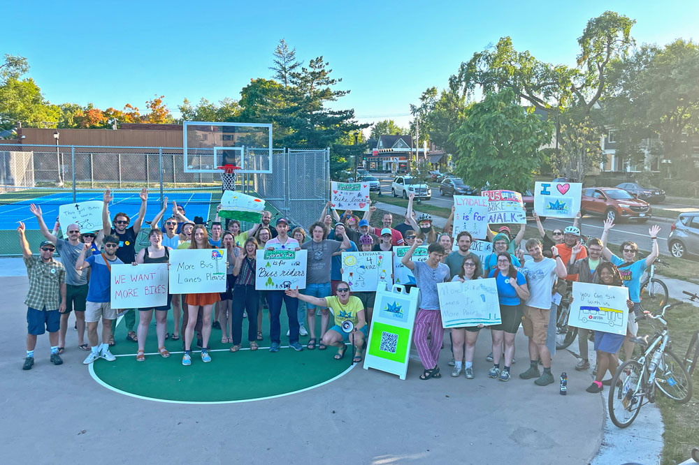 A large group of advocates pose with signs for a Livable Lyndale on a basketball court in Minneapolis' Painter Park