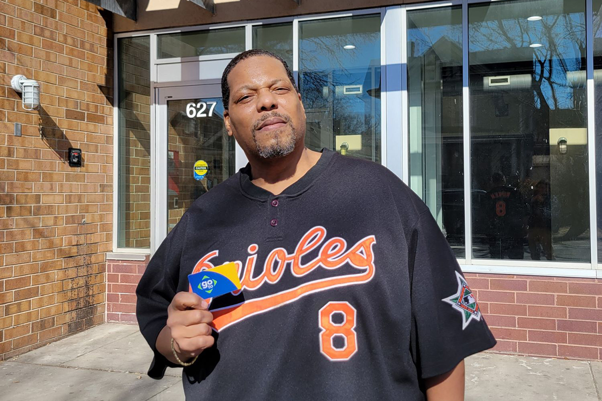 Anthony, a Black man with a graying goatee, wearing a dark blue Orioles shirt and holding a Go-To Card for Metro Transit