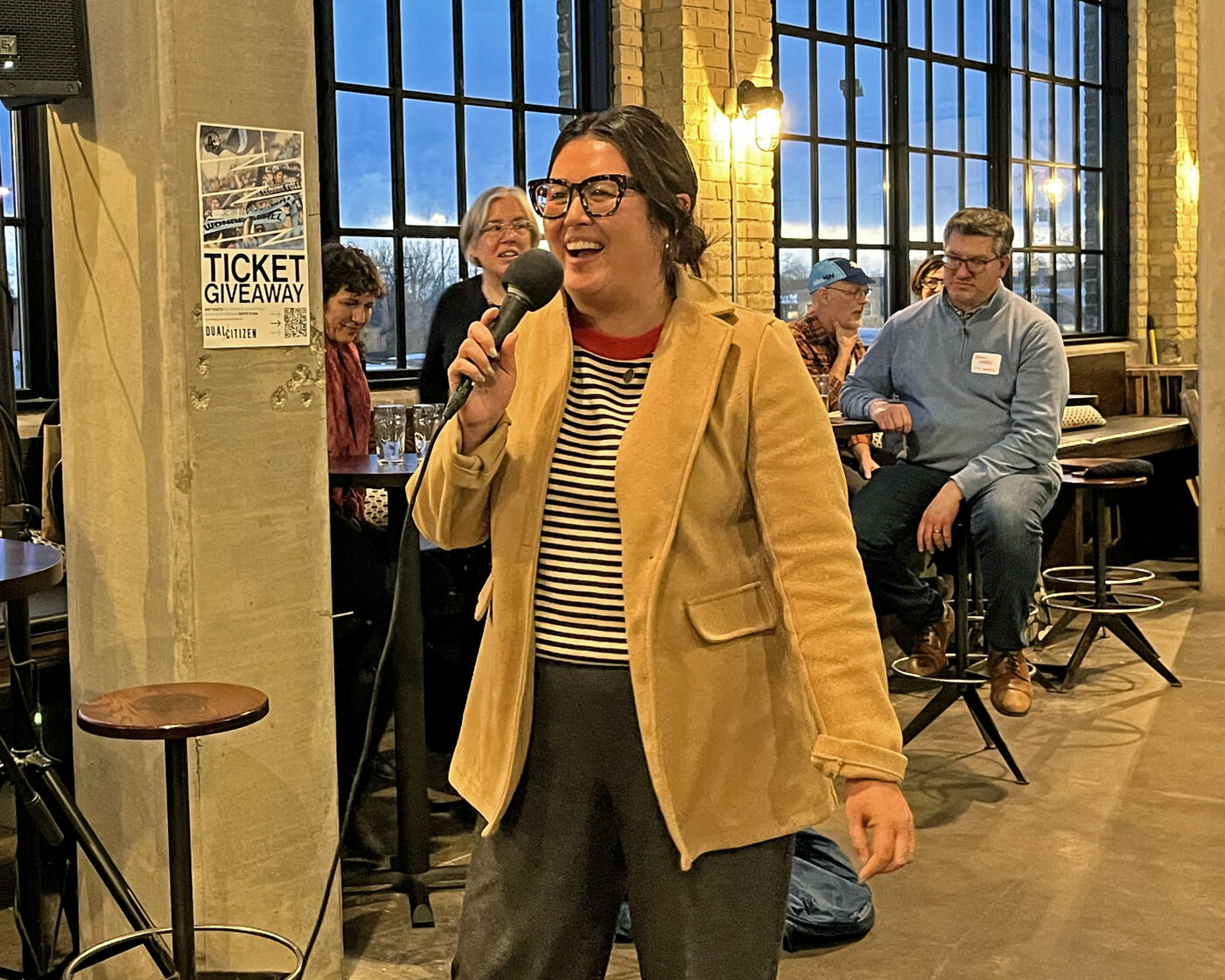 Rep. Samantha Sencer-Mura, an olive-skinned woman wearing cat-eye glasses and a black-striped shirt, gives words of encouragement to advocates to continue bringing a positive vision to the capitol